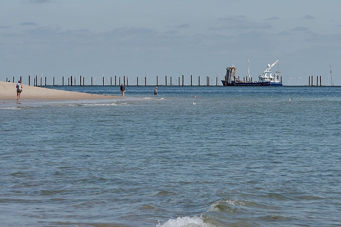 Reihe hoher Pfähle und Fangschiff vor Sylt