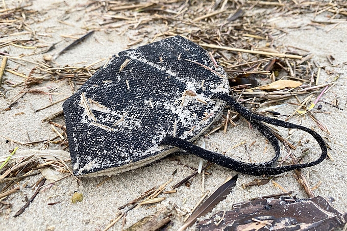 Am Strand angespülte schwarze Coronamaske 