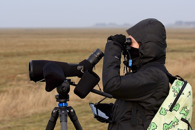 Freiwillige in Handschuhen und Schal am Fernglas