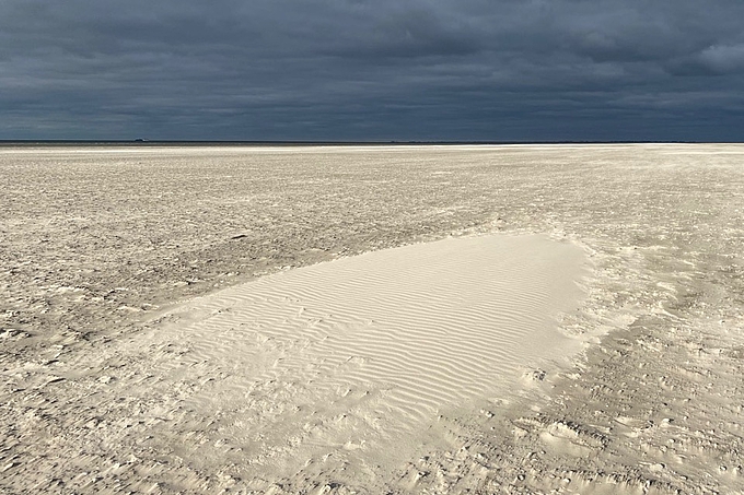 Sonniger Sand vor dunklen Wolken