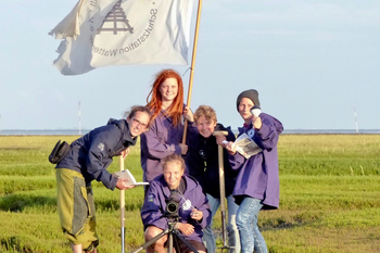 Freiwilligen-Team Schutzstation Wattenmeer mit Flagge und Arbeitsgeräten