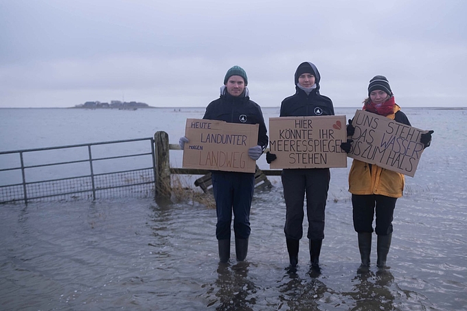 Drei Freiwillige mit Plakaten bei Landunter auf der Hallig