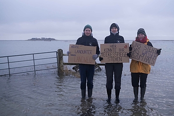 Drei Freiwillige mit Plakaten bei Landunter auf der Hallig