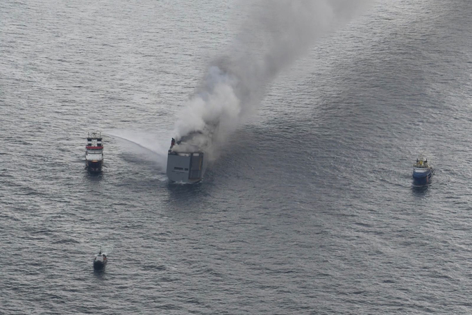 Brennender Frachter mit mehreren Hilfsschiffen in der Nähe