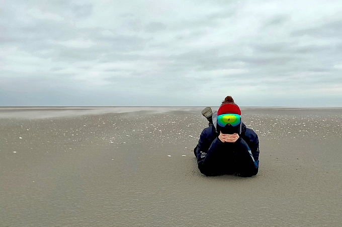 Freiwillige liegt dick vermummt auf der Sandbank