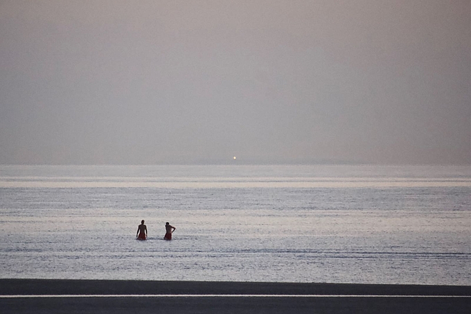 Badende am Ordinger Strand mit dem Licht des Helgoländer Leuchtturms 