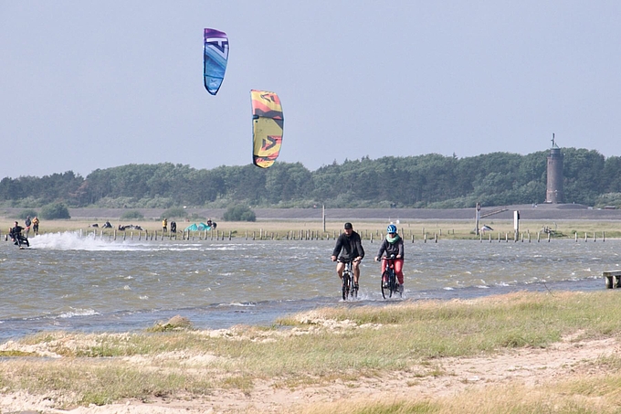 Radfahrer und Kitesurfer in flachem Wasser