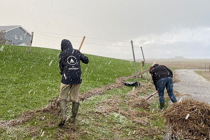 Zwei Personen schieben bei Schneefall Treibgut zusammen