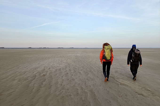 Zwei Freiwillige laufen über hohes Sandwatt zur Hallig