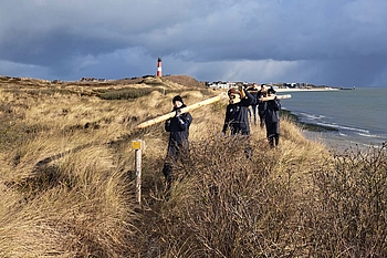 Gruppe von Freiwilligen trägt Holzpfähle durch Dünen