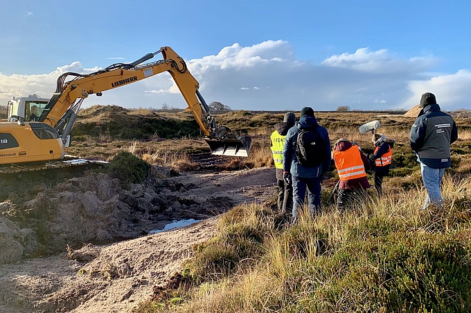 Bagger und Personen in den Dünen