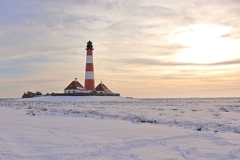 Leuchtturm im Sonnenlicht in verschneiter Salzwiese