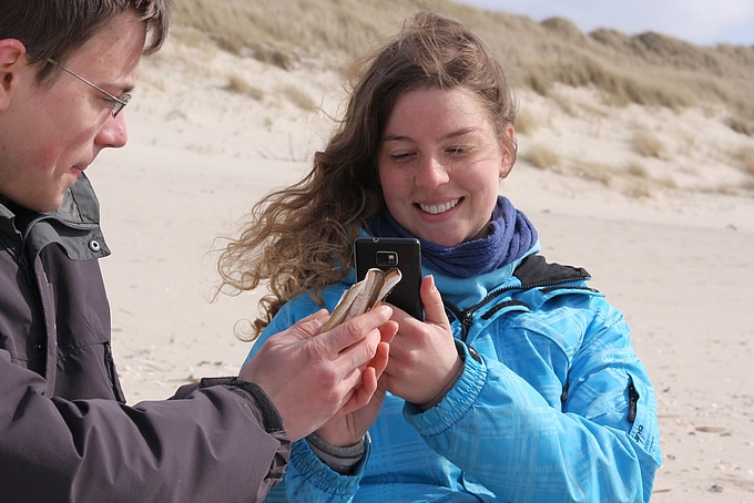 Zwei Personen mit Handy und Muscheln Zwei Personen mit Handy und Muscheln