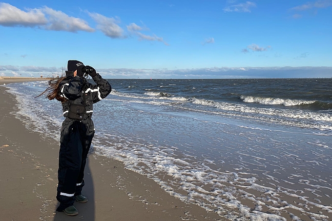 Freiwillige in Wetterkleidung blickt mit dem Fernglas auf die See