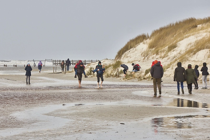 Wanderer waten barfuß vor Dünen