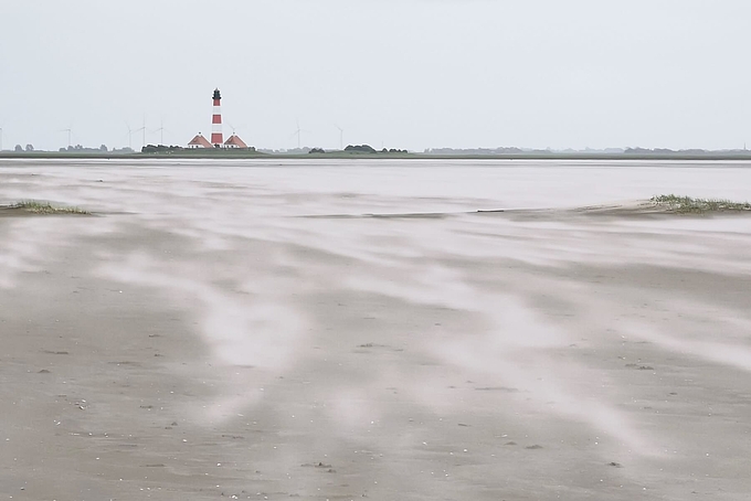 Blick zum Leuchtturm über fliegendem Sand