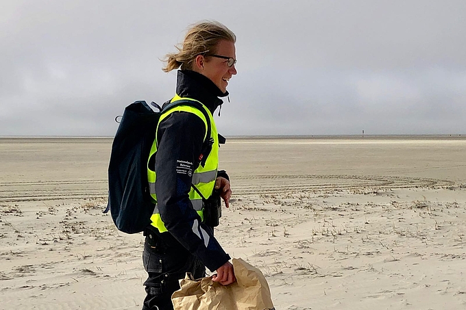 Freiwilliger mit Müllsack am Rand der Dünen